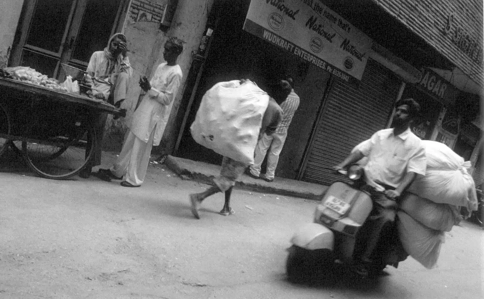 Fotografía en blanco y negro de una calle de nueva delhi en la India. Motocicleta repartiendo sacos