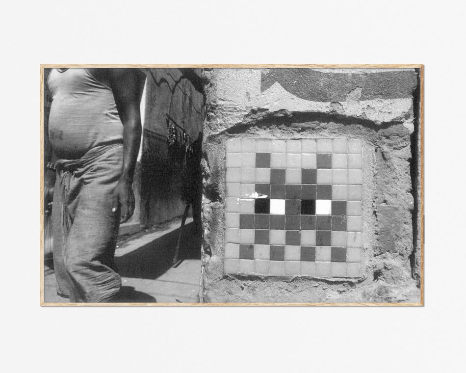 Lámina blanco y negro foto de un indio frente a un mosaico del artista urbano Space Invaders en Varanasi, India