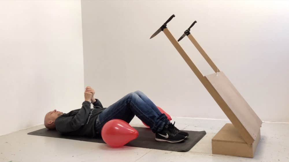 Fotografia del artista jan erichsen explotando dos globos con uno de sus inventos