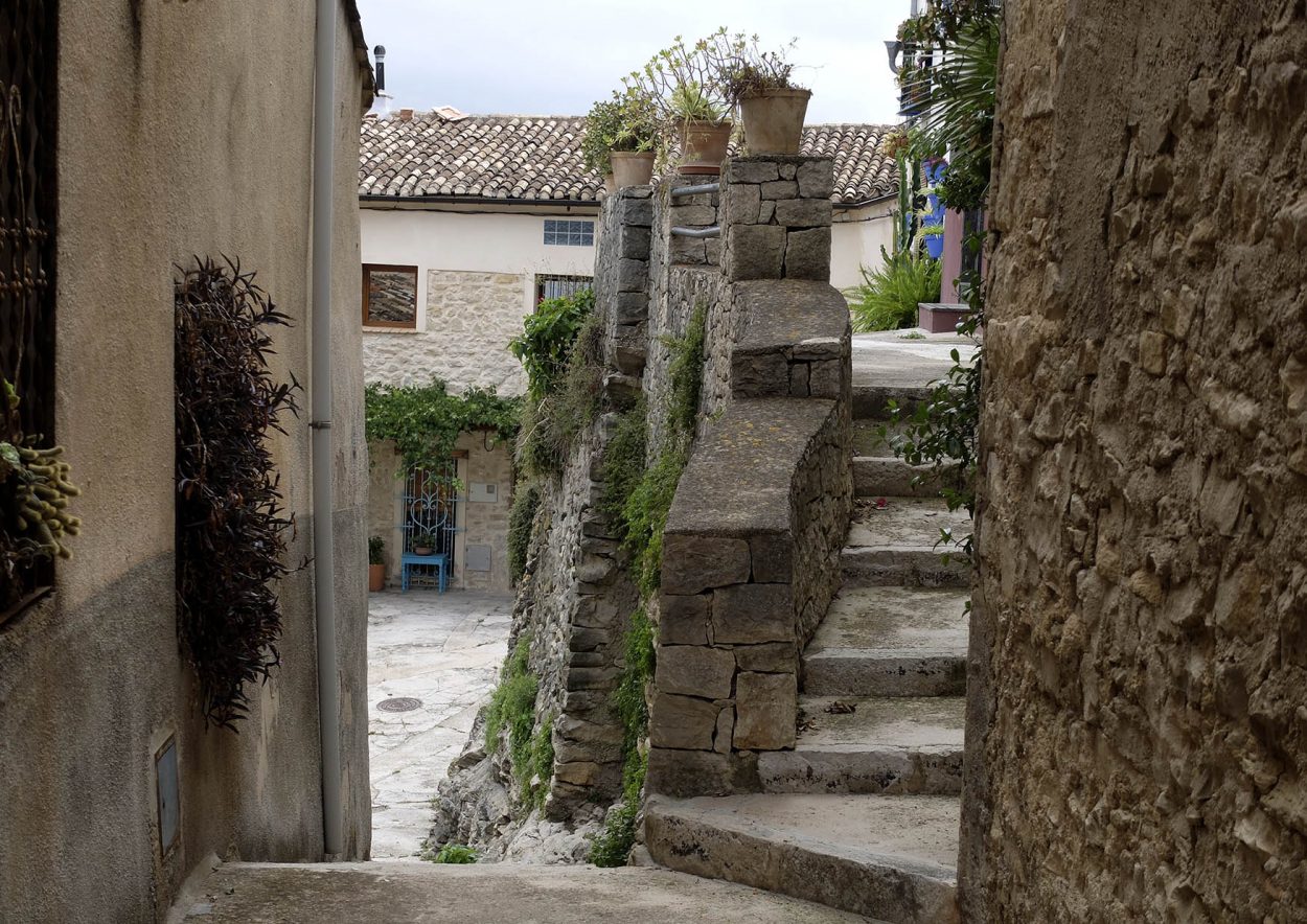 Fotografía de una calle empedrada, casas y una escalera en la Carrotja, Vall de la Gallinera.